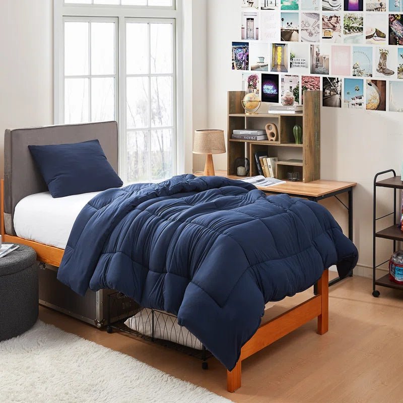 Navy blue twin XL bedding set neatly arranged on a dorm room bed, including a comforter and pillow.