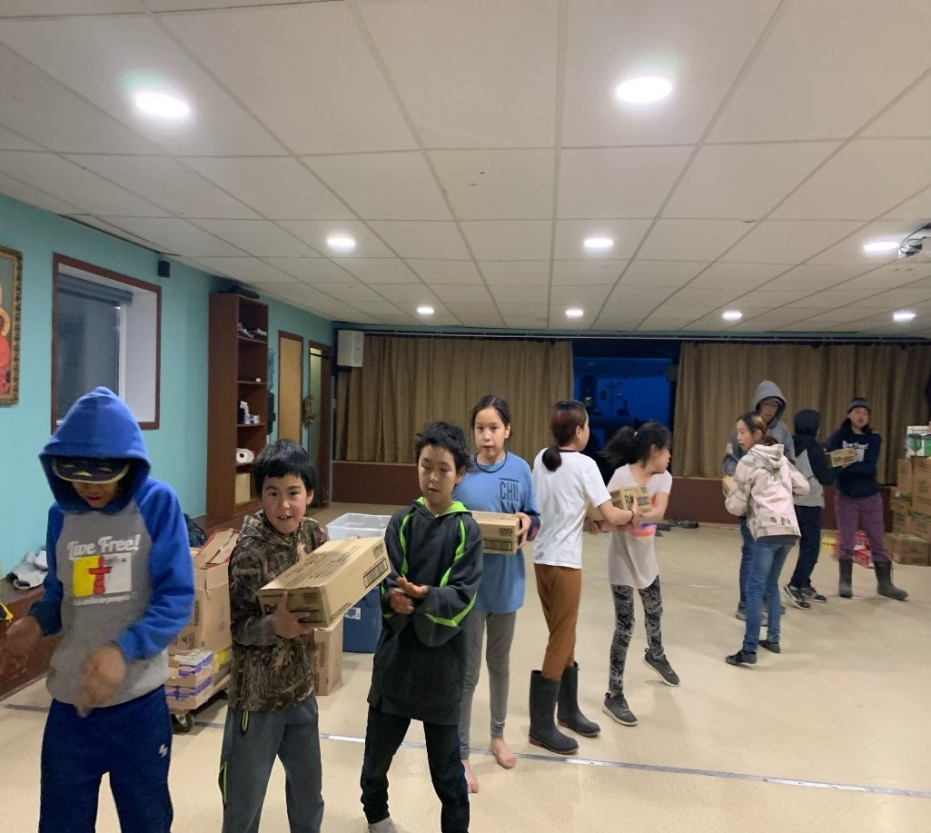 Young people carry boxes through a community hall